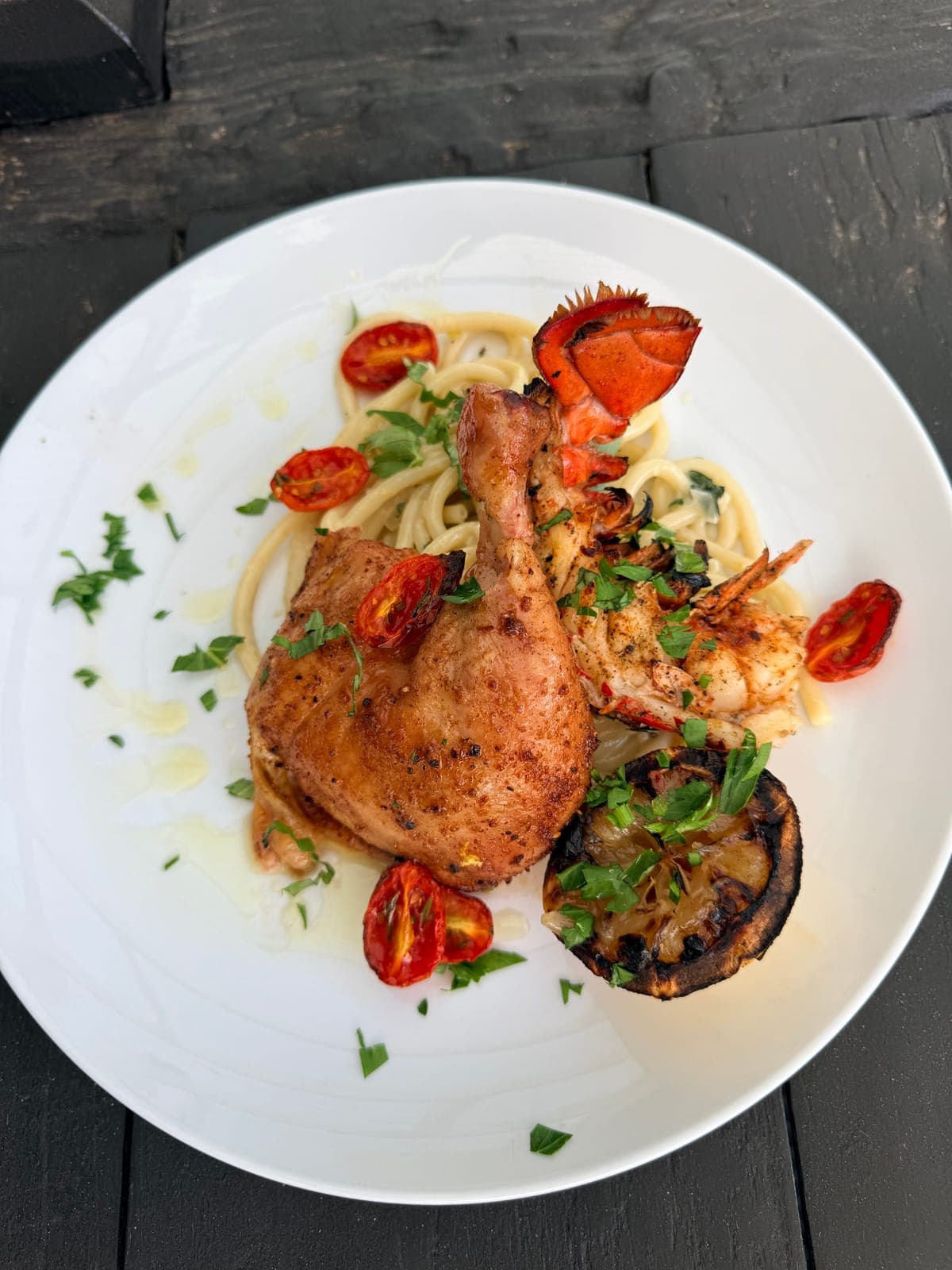 Roasted chicken and grilled lobster tail over pasta with blistered tomatoes